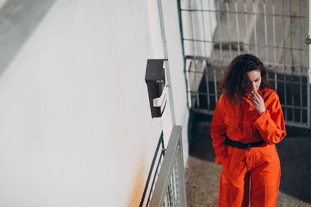 Young prisoner woman in orange suit at jail smoking Female in colorful overalls portrait