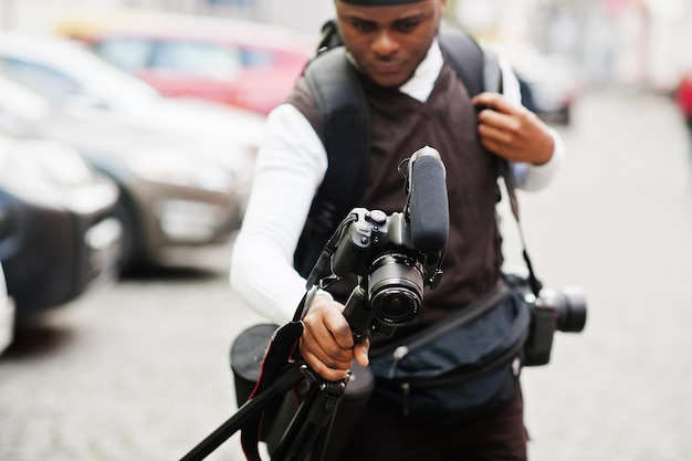 Young professional african american videographer holding professional camera with tripod pro equipment Afro cameraman wearing black duraq making a videos