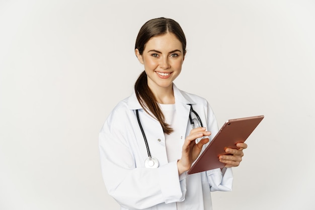 Young professional doctor woman physician with stethoscope holding digital tablet and smiling at cam...