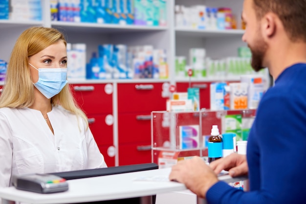 Young professional druggist give medications to customer in modern drugstore