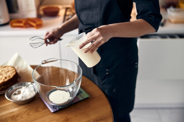 Young professional female cook is preparing tasty cake at her light modern kitchen