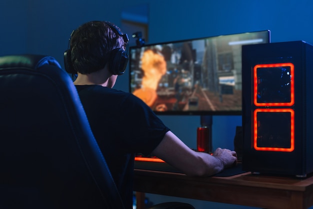 Young professional gamer playing tournaments online video games on computer with headphones in his room