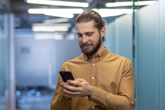 Photo a young professional man with a beard engaged in using his smartphone stands in a contemporary