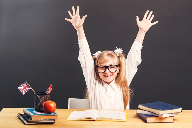 Photo young pupil girl wears smart eyeglasses rise hands up learning english language with book before dark background