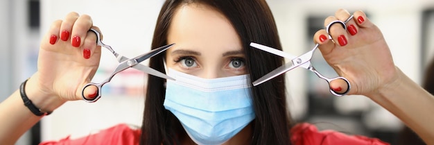 Young qualified master holding pair of scissors for work and posing in face mask