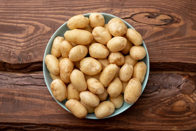 Young raw potatoes small on a plate on a brown wooden background.