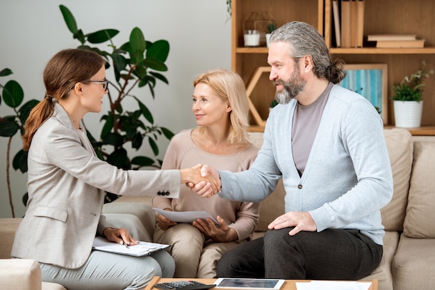 Young real estate agent congratulating mature couple with buying new house after signing documents