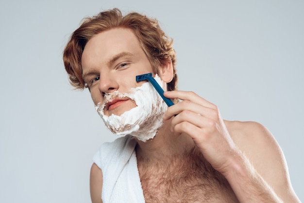 Young red haired guy neatly shaves with razor. Male hygiene.