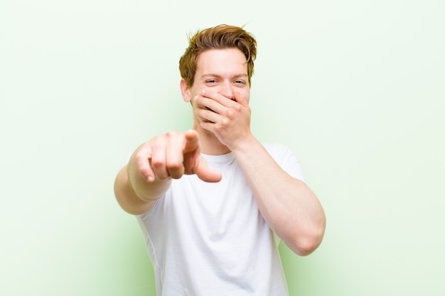 Young red head handsome man laughing at you, pointing and making fun of or mocking you