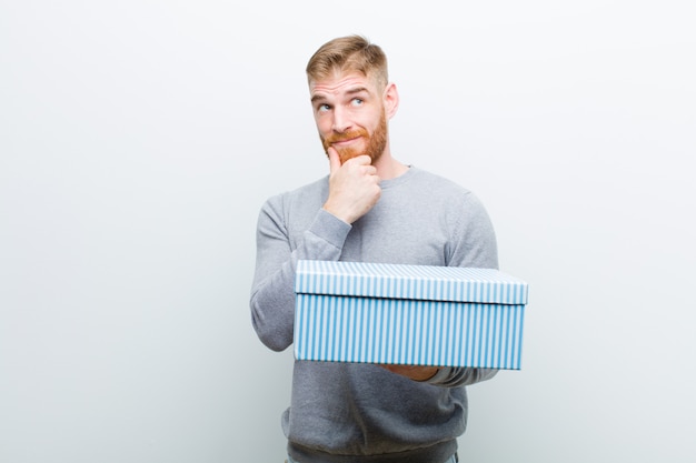 Young red head man holding a gift box on white