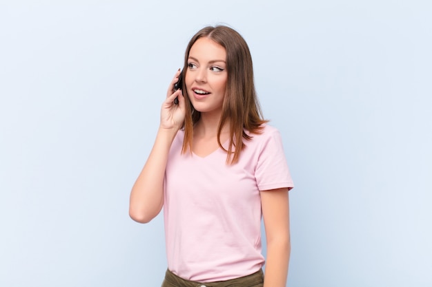 Young red head woman  against flat wall with a smart phone