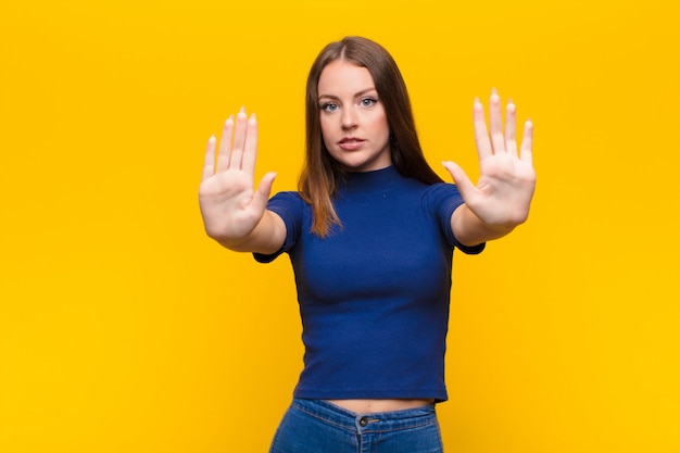 Young red head woman looking serious, unhappy, angry and displeased forbidding entry or saying stop with both open palms