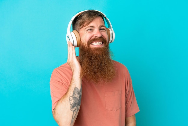 Young reddish caucasian man isolated on blue background listening music