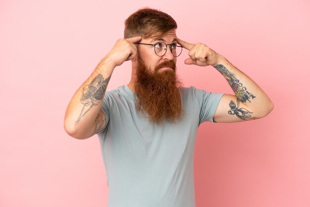 Young reddish caucasian man isolated on pink background having doubts and thinking