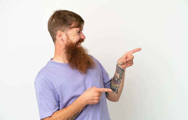 Young reddish caucasian man isolated on white background pointing finger to the side and presenting a product