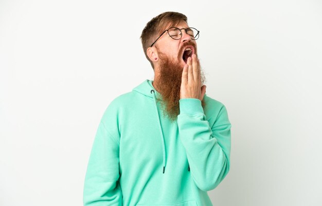 Young reddish caucasian man isolated on white background yawning and covering wide open mouth with hand