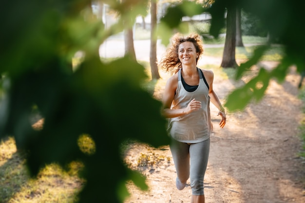 Young redhaired woman runs a marathon outdoors in a city park in the forest warm rays of the sun