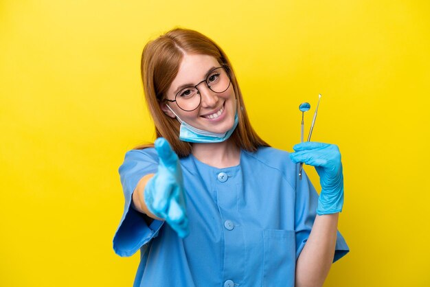 Young redhead Dentist woman isolated on yellow background shaking hands for closing a good deal