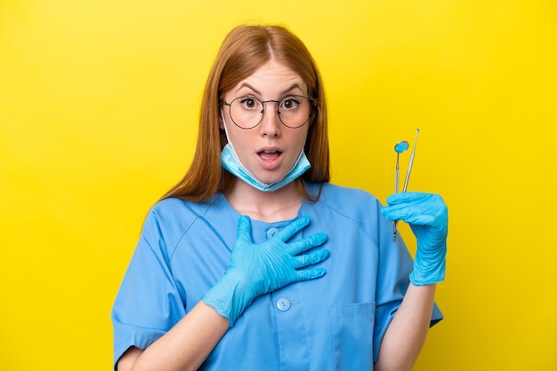 Young redhead Dentist woman isolated on yellow background surprised and shocked while looking right