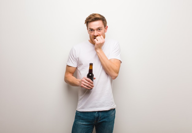 Young redhead man biting nails, nervous and very anxious