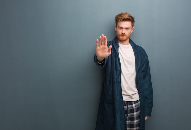 Young redhead man in pajama putting hand in front