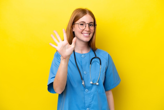 Young redhead nurse woman isolated on yellow background counting five with fingers