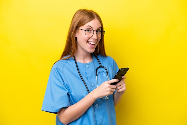 Young redhead nurse woman isolated on yellow background surprised and sending a message