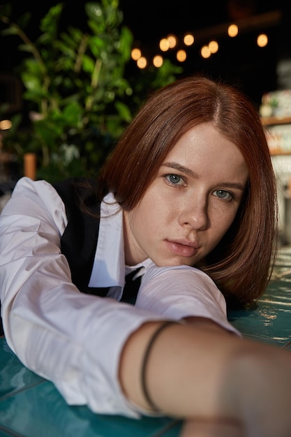 Young redhead pretty girl with long hair lays her head on her arms and table