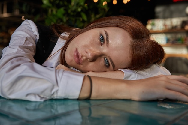 Young redhead pretty girl with long hair lays her head on her arms and table