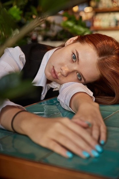 Young redhead pretty girl with long hair lays her head on her arms and table