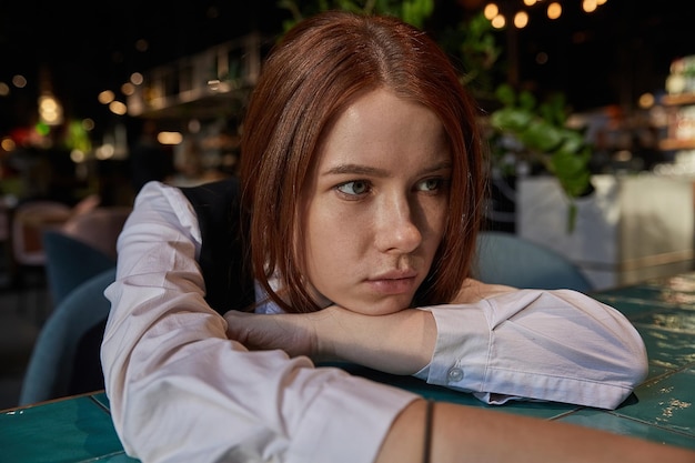 Young redhead pretty girl with long hair lays her head on her arms and table