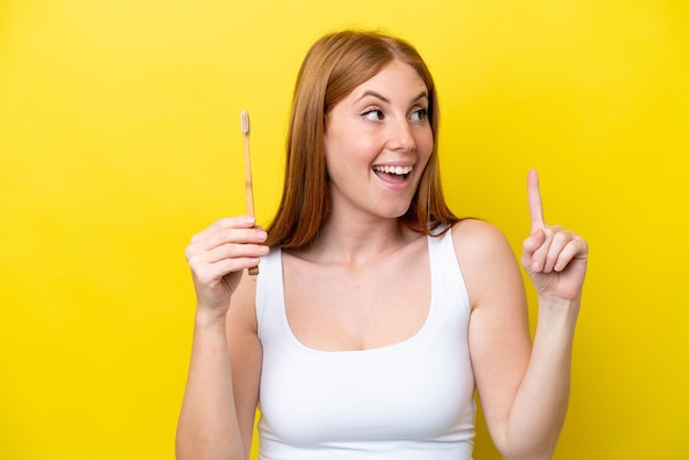 Young redhead woman brushing teeth intending to realizes the solution while lifting a finger up