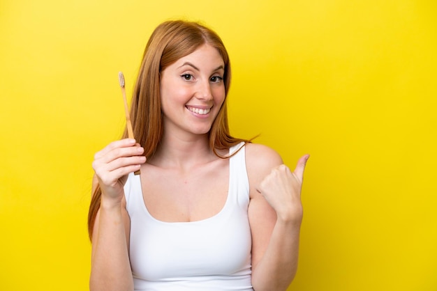 Young redhead woman brushing teeth pointing to the side to present a product