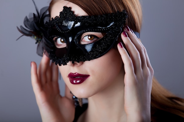 Young redhead woman in carnival mask on grey