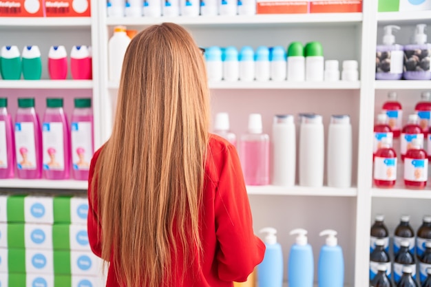 Young redhead woman customer looking shelving at pharmacy