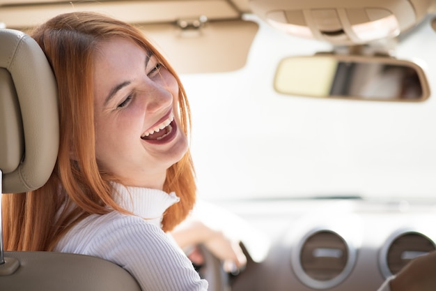 Young redhead woman driver driving a car smiling happily.