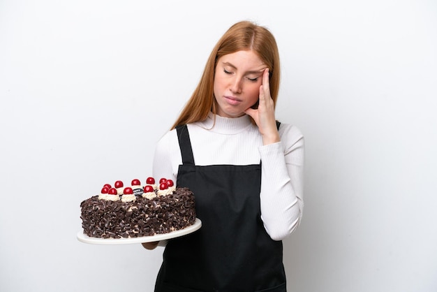 Young redhead woman holding birthday cake isolated on white background with headache