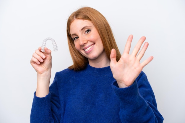 Young redhead woman holding invisible braces isolated on white background saluting with hand with happy expression