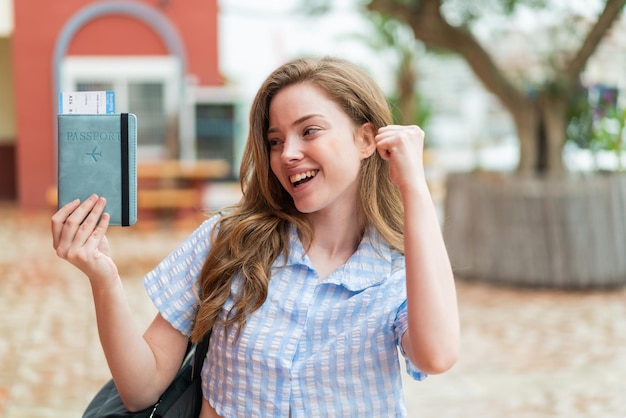 Young redhead woman holding a passport at outdoors celebrating a victory