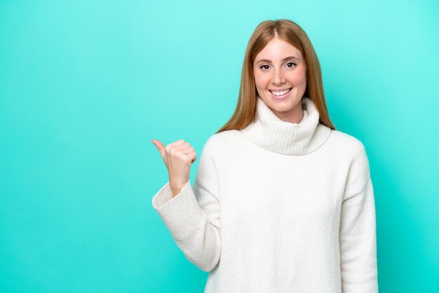 Young redhead woman isolated on blue background pointing to the side to present a product