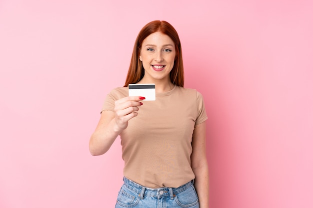 Young redhead woman over isolated  holding a credit card