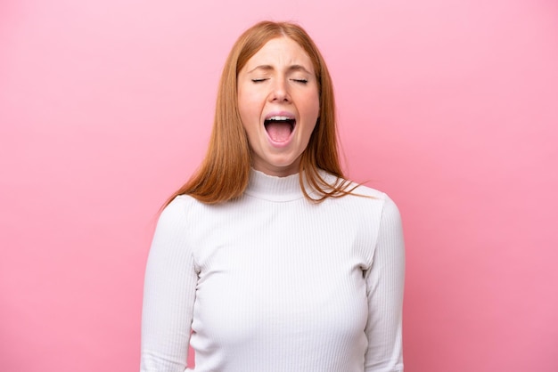 Young redhead woman isolated on pink background shouting to the front with mouth wide open