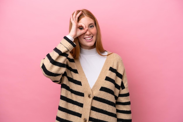 Young redhead woman isolated on pink background showing ok sign with fingers