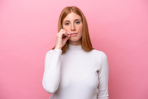 Young redhead woman isolated on pink background showing a sign of silence gesture