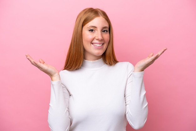 Young redhead woman isolated on pink background with shocked facial expression