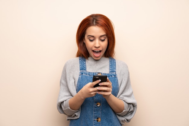 Young redhead woman over isolated  surprised with a mobile