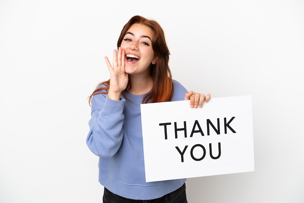 Young redhead woman isolated on white background holding a placard with text THANK YOU and shouting