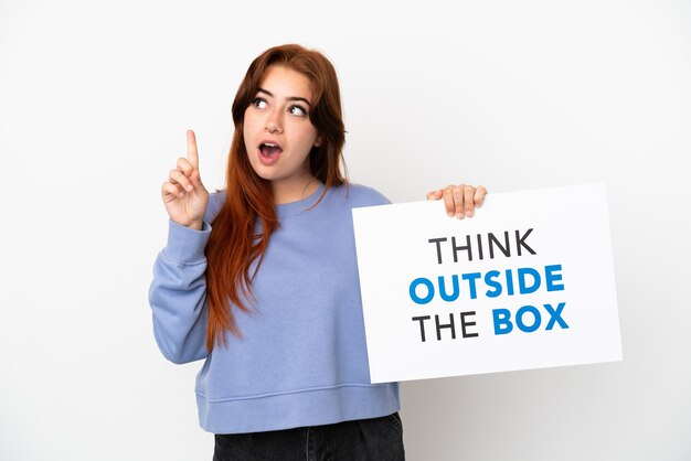 Photo young redhead woman isolated on white background holding a placard with text think outside the box and thinking