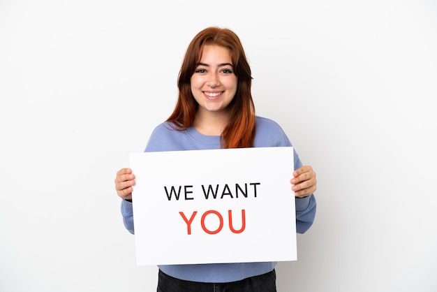 Young redhead woman isolated on white background holding We Want You board with happy expression