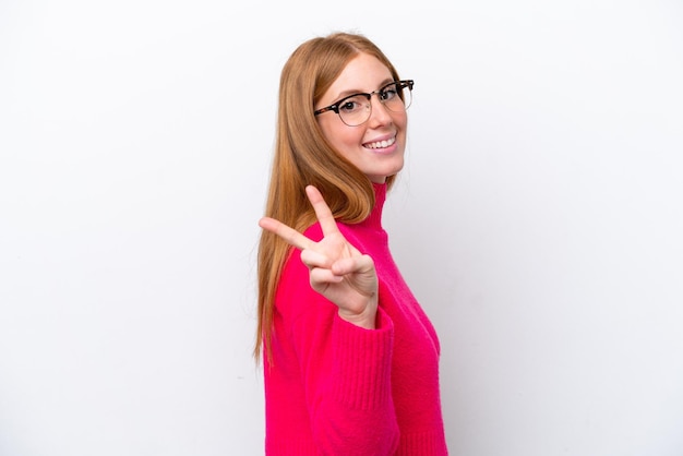 Young redhead woman isolated on white background smiling and showing victory sign